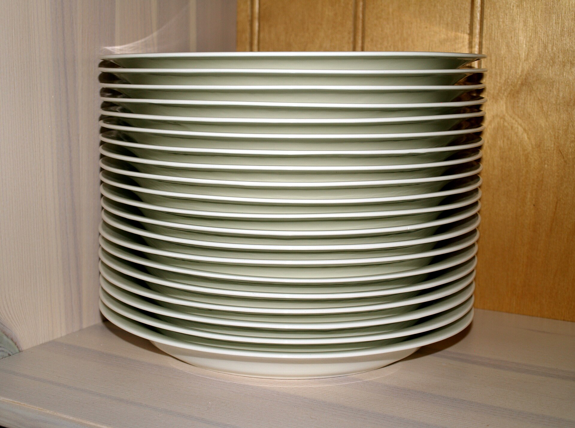 A tall stack of identical white dinner plates on a wooden shelf